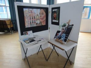 Two tables infront of large standing canvases displaying GCSE artwork