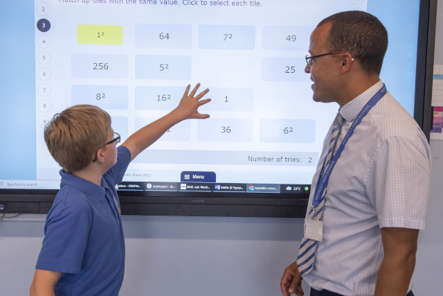 Astudent solving a maths puzzle on an interactive TV screen with his teacher next to him
